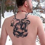 Фото тату на спине мужчины: череп оленя с рогами, обвитый змеями, в стиле blackwork. Детализированный рисунок татуировки.