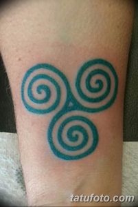 Фото тату с изображением зеленого кельтского трилистника (трикветра) на предплечье. Детализированный рисунок татуировки с использованием ярких цветов.
