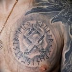 Фото тату: изображение коловрата, окруженного рунами, на груди. Детализированная проработка символов и узоров.