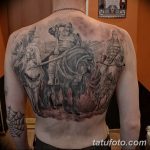 Фото тату на спине мужчины с изображением сцены битвы. Изображены воины на лошадях, оружие и элементы пейзажа.