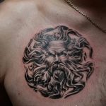 Фото тату на груди: реалистичное изображение головы морского бога с длинной бородой и волнами, выполненное в черно-серых тонах. Детализированный рисунок татуировки.