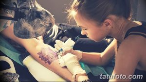 Фото процесса нанесения татуировки: мастер в перчатках делает тату на руке клиента. Видна тату-машинка и эскиз.
