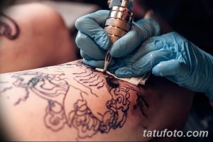 Фото процесса нанесения татуировки: мастер в голубых перчатках работает тату-машинкой над эскизом на коже клиента. Виден контур рисунка.