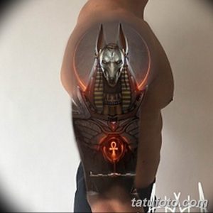 Фото тату с изображением Анубиса, египетского бога с головой шакала, выполненное в ярких цветах с использованием оранжевого и черного. Татуировка расположена на спине.