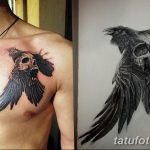 Фотография татуировки на груди, изображающей ворона, сидящего на человеческом черепе. Рисунок выполнен в стиле реализм с высокой детализацией и использованием черно-серых оттенков.