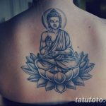Фото тату: изображение Будды, сидящего в позе лотоса на фоне цветка лотоса, выполненное в черно-серых тонах на спине девушки. Детализированный рисунок.