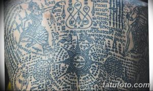Фото тату на спине: сложный узор из сакральных символов, геометрических фигур и надписей, выполненный в черном цвете.