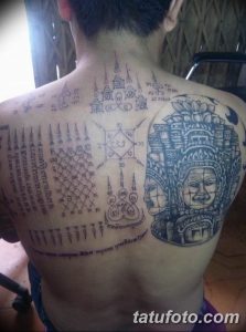 Фото тату: сложный узор тайских сакральных символов и иероглифов на спине мужчины. Детализированный рисунок татуировки в черном цвете.
