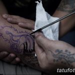 Фото процесса нанесения татуировки на стопу, выполненной в стиле традиционного тайского рисунка. Мастер тату наносит рисунок с помощью ручного инструмента.