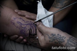Фото процесса нанесения татуировки на стопу, выполненной в стиле традиционного тайского рисунка. Мастер тату наносит рисунок с помощью ручного инструмента.