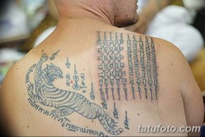 Фото тату на спине с изображением тигра и тайскими письменами. Татуировка выполнена в черных тонах и имеет сложную структуру.