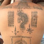 Фото тату: большая татуировка на спине, покрытая сложными узорами, изображениями животных и религиозными символами. Традиционный тайский стиль.