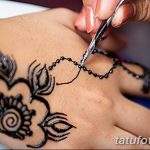 Фото процесса нанесения мехенди (временной татуировки хной) на руку. Мастер аккуратно наносит сложный узор с использованием специальной пасты.