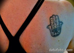 Фото минималистичной татуировки Хамса на плече. Черно-белый рисунок с тонкими линиями и небольшим размером.