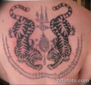 Фото татуировки на спине с изображением двух тигров, защитных символов и священных текстов. Черно-серый рисунок в тайском стиле.