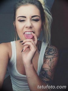 Фото тату: большая черная роза с зелеными листьями на предплечье девушки. Реалистичный рисунок татуировки с детальной проработкой лепестков.