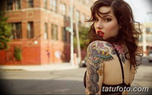 Фотография девушки с ярким рукавом татуировок на плече. На татуировке изображены бабочки, цветы и другие элементы в ярких и насыщенных цветах.