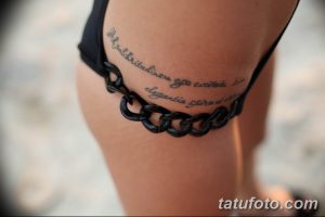 Фотография татуировки на бедре девушки. Это длинная надпись, выполненная изящным шрифтом, обвивающая бедро. Рядом с надписью изображена цепочка.