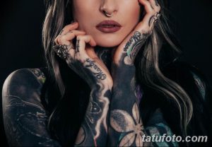 Фотография девушки с множеством татуировок на руках и шее. Татуировки включают в себя цветы, бабочек, надписи и абстрактные узоры, выполненные в черных и серых тонах.