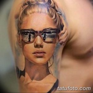 Фотография реалистичной татуировки с изображением девушки в солнцезащитных очках. Татуировка выполнена на плече, с высокой детализацией и реалистичной передачей черт лица.