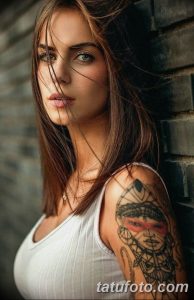 Фотография девушки с татуировкой в виде лица на плече, выполненной в геометрическом стиле.