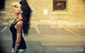 Фотография девушки с длинными темными волосами и татуировкой в виде цветочного рукава на правой руке, демонстрирующая красоту и детализацию рисунка.