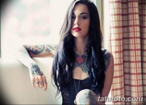 Фотография девушки с длинными темными волосами и множеством татуировок на руках и шее, демонстрирующая разнообразие рисунков татуировок.