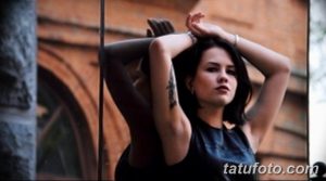 Фото тату на предплечье девушки с темными волосами. Изящная надпись черным цветом, минималистичный стиль, акцент на красоте линий.