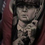 Фото тату с изображением Томаса Шелби из сериала 'Пики Бларди', курящего сигарету, выполненное в реалистичном черно-белом стиле на руке.