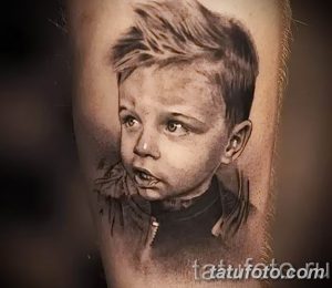 Фотография татуировки с реалистичным портретом маленького мальчика, выполненной в черно-серых тонах на руке.