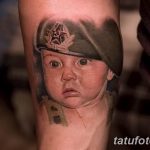 Фото татуировки с изображением младенца в военной фуражке, выполненной в ярком и реалистичном стиле на руке. Необычный и юмористический рисунок.