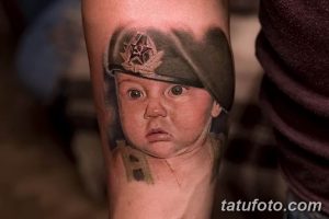 Фото татуировки с изображением младенца в военной фуражке, выполненной в ярком и реалистичном стиле на руке. Необычный и юмористический рисунок.