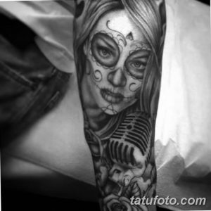 Фото тату: черно-белая татуировка в стиле Sugar Skull на руке. Изображение девушки с черепом, украшенной цветами и микрофоном.