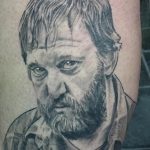 Фотография татуировки на руке с изображением портрета мужчины с бородой и серьезным выражением лица, выполненного в реалистичном стиле.