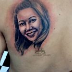 Фотография татуировки на груди с изображением портрета молодой девушки с улыбкой, выполненного в реалистичном стиле.