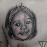 Фото тату: черно-белый портрет ребенка на груди, выполненный в реалистичном стиле. Трогательный и личный рисунок, символизирующий любовь и память.