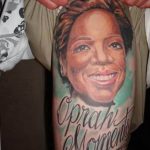 Фото тату: реалистичный портрет Опры Уинфри на предплечье, с надписью 'Oprah's Moments' и бирюзовым фоном. Идеально для поклонников медиа-персоны.