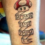 Фото тату персонажа Марио из игры Super Mario с надписями 'Играй', 'Или', 'Умри' на ноге. Рисунок татуировки выполнен в черном цвете.