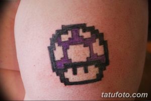 Фото тату с изображением пиксельного блока из игры Minecraft на руке. Татуировка выполнена в черно-фиолетовом цвете, с использованием характерных для игры пикселей.