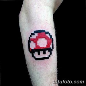 Фото татуировки в стиле пиксель-арт с изображением гриба Super Mushroom из игры Super Mario Bros. Татуировка выполнена в красном и белом цветах.