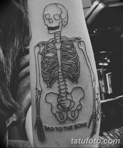 Фото тату: простой рисунок скелета на руке с надписью "BAD TO THE BONE", выполненный в стиле олдскул.