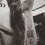 Фото тату: изображение скелета, выполненное тонкими линиями на руке, с надписью на французском языке. Лаконичный и стильный эскиз татуировки.