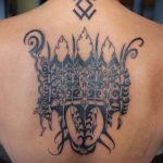 Фото тату: Большая татуировка в стиле трайбл, покрывающая спину, с изображением воина и символов. Детализированный рисунок татуировки.