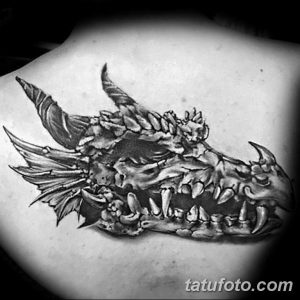 Фото тату: стилизованная голова дракона, выполненная в технике blackwork на лопатке. Эскиз тату с акцентом на темные тона.