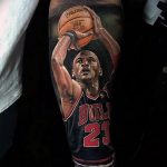 Фото тату с изображением Майкла Джордана в форме Chicago Bulls, держащего баскетбольный мяч. Реалистичный портрет на предплечье.