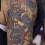 Фото тату на руке с изображением игрока в американский футбол, логотипов NFL и стадиона Gillette Stadium. Детализированный рисунок татуировки.
