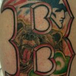 Фото тату на руке с изображением буквы 'B' и головы медведя. Яркий рисунок с использованием различных цветов.