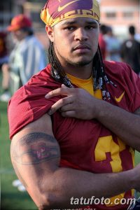 Фото тату на плече с изображением логотипа команды USC Trojans. Рисунок выполнен в черно-серых тонах с использованием контуров.