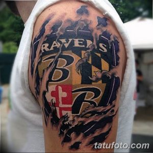 Фото тату на плече с изображением логотипа команды Baltimore Ravens в ярких цветах: черном, золотом и красном. Детализированный рисунок татуировки.