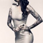 Фотография девушки в облегающем сером платье, демонстрирующей татуировки на руках, ногах и шее.